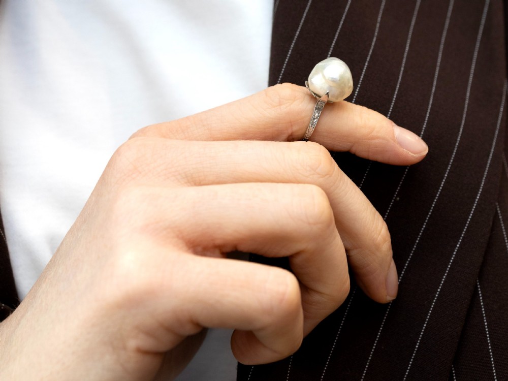 An antique platinum dress ring featuring a large, smooth natural blister pearl flanked by diamond-set shoulders. View VII