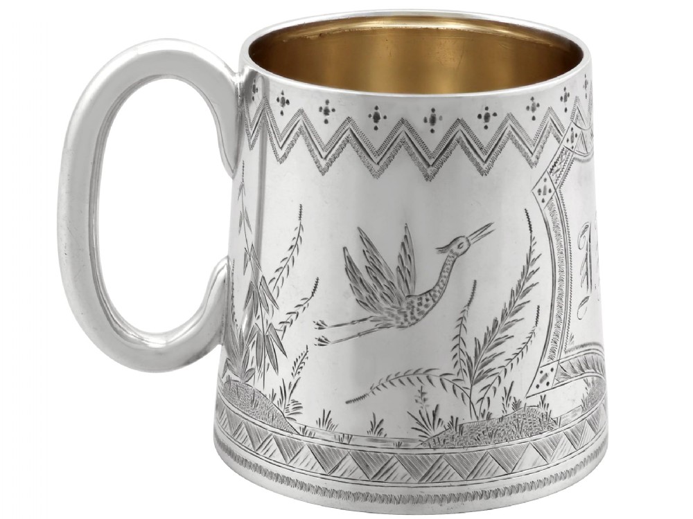 A tapered sterling silver christening mug featuring hand-engraved foliage and bird motifs, geometric borders, a loop handle, and a gilt interior.
