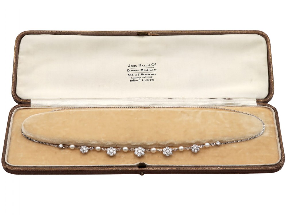 An Edwardian platinum chain necklace set with diamond floral clusters and interspersed with round white pearls.