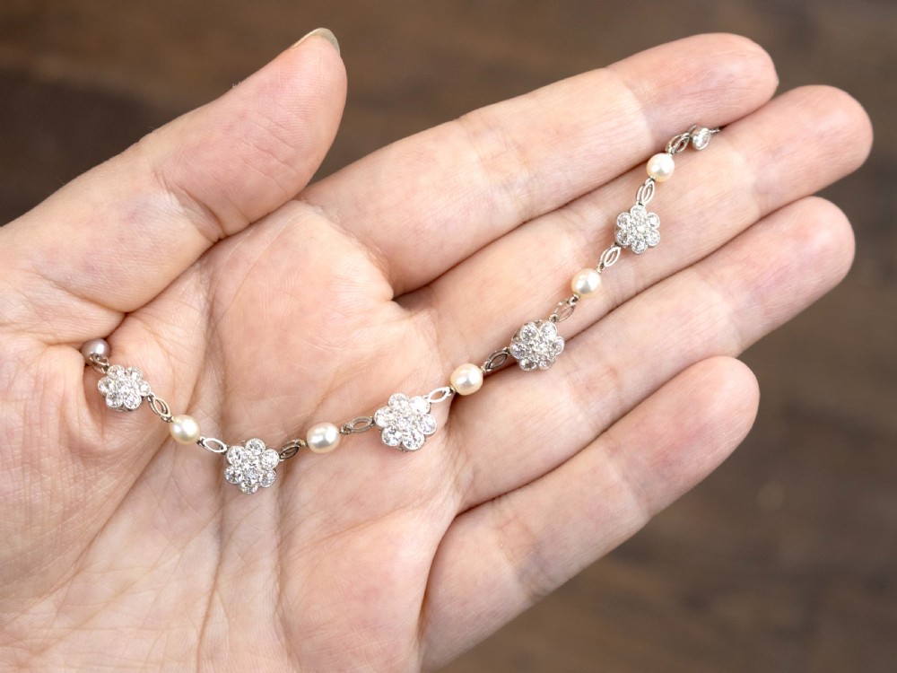 An Edwardian platinum chain necklace set with diamond floral clusters and interspersed with round white pearls. View IV