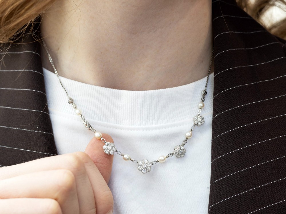 An Edwardian platinum chain necklace set with diamond floral clusters and interspersed with round white pearls. View V
