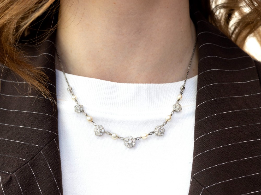 An Edwardian platinum chain necklace set with diamond floral clusters and interspersed with round white pearls. View VI