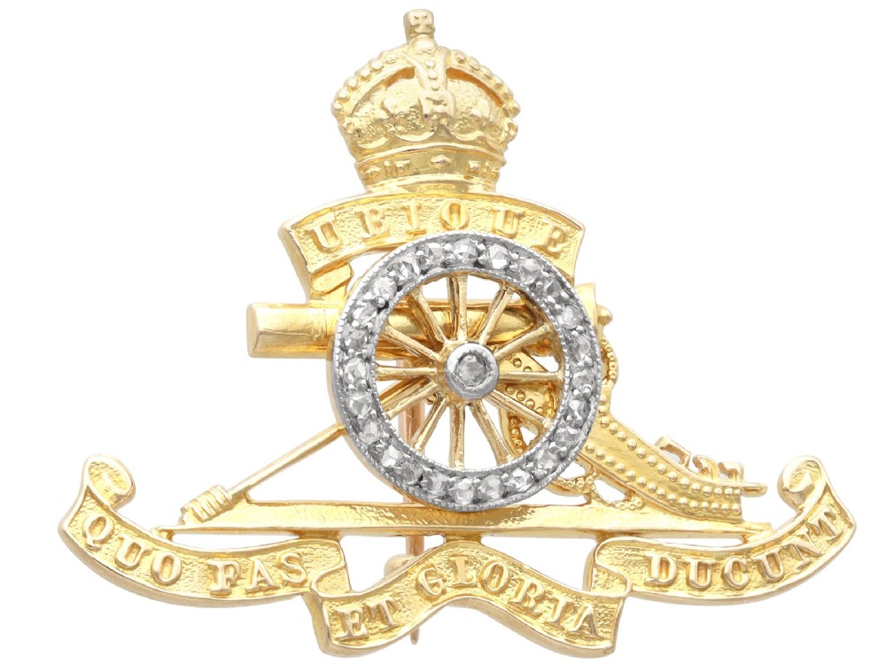 An 18ct yellow gold Royal Artillery brooch featuring a diamond-set gun wheel, crowned cannon motif, and Latin motto ribbons.