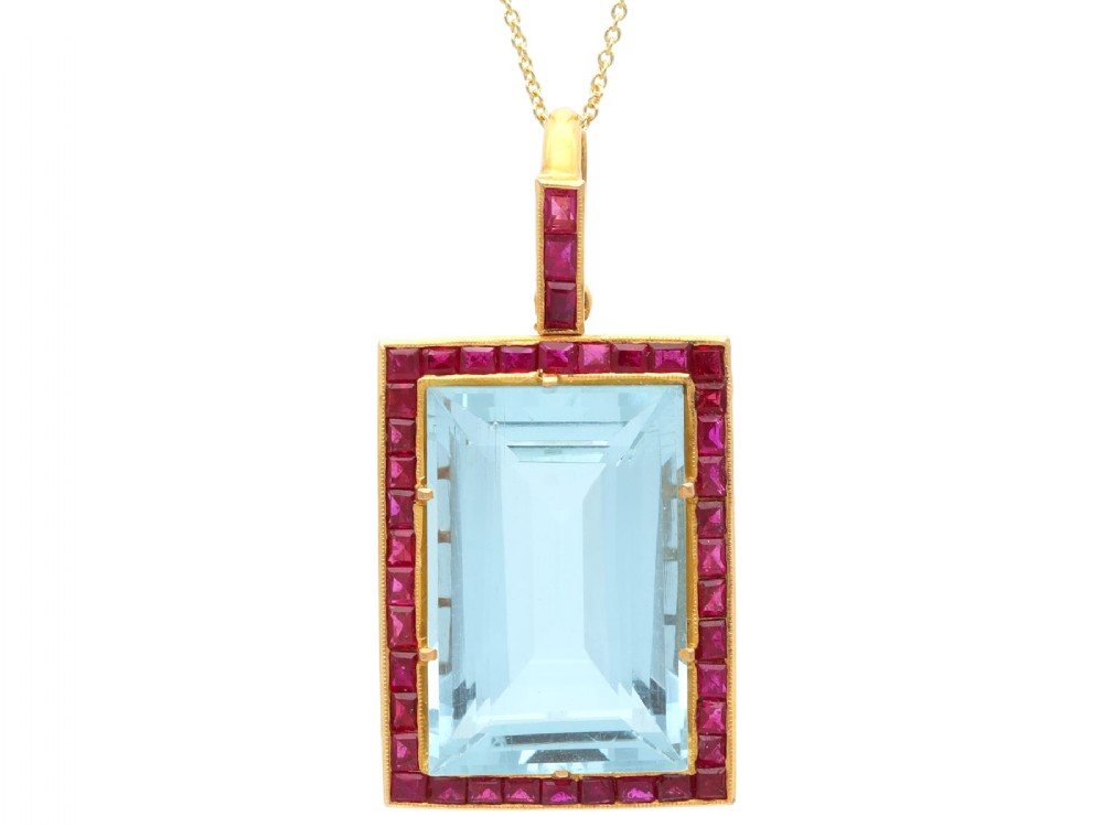 A large rectangular step-cut blue aquamarine set in yellow gold with a square-cut red ruby border and ruby-set bail.