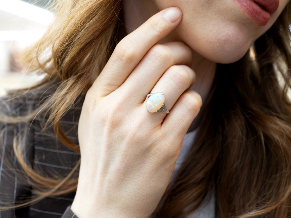 An Art Deco 18ct white gold ring featuring a central oval cabochon white opal flanked by geometric diamond-set shoulders. View III