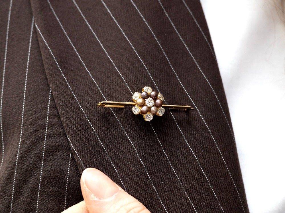 An antique 15ct yellow gold bar brooch featuring a central floral cluster set with dark pearls and old-cut diamonds. View V