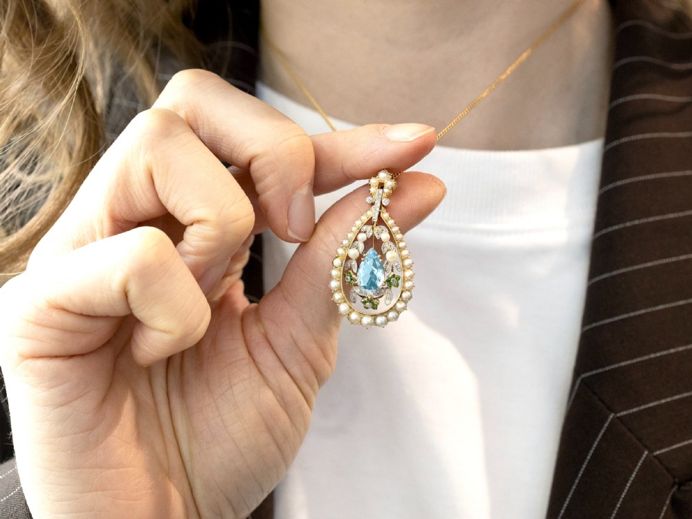 An openwork Edwardian 14ct yellow gold pendant set with a central pear-cut aquamarine surrounded by seed pearls, diamonds, and green demantoid garnets. View IV