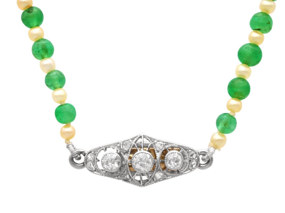 An antique single strand necklace displaying alternating green emerald beads and cream pearls connected to a geometric platinum and diamond clasp.