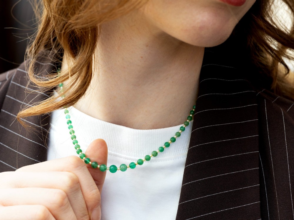An antique single strand necklace displaying alternating green emerald beads and cream pearls connected to a geometric platinum and diamond clasp. View VI