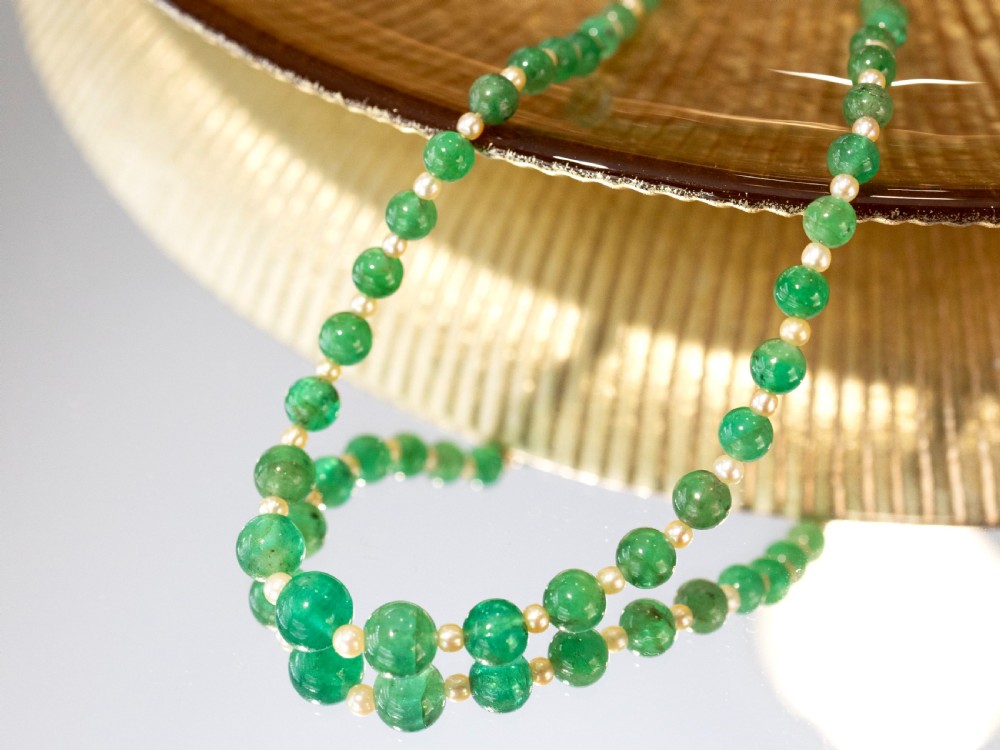 An antique single strand necklace displaying alternating green emerald beads and cream pearls connected to a geometric platinum and diamond clasp. View IX