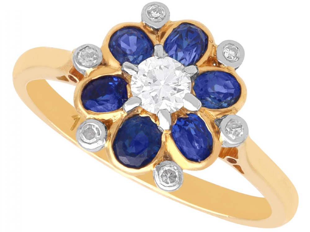An 18ct yellow gold ring featuring a central round diamond surrounded by six oval blue sapphires and outer round diamond accents arranged in a flower motif.