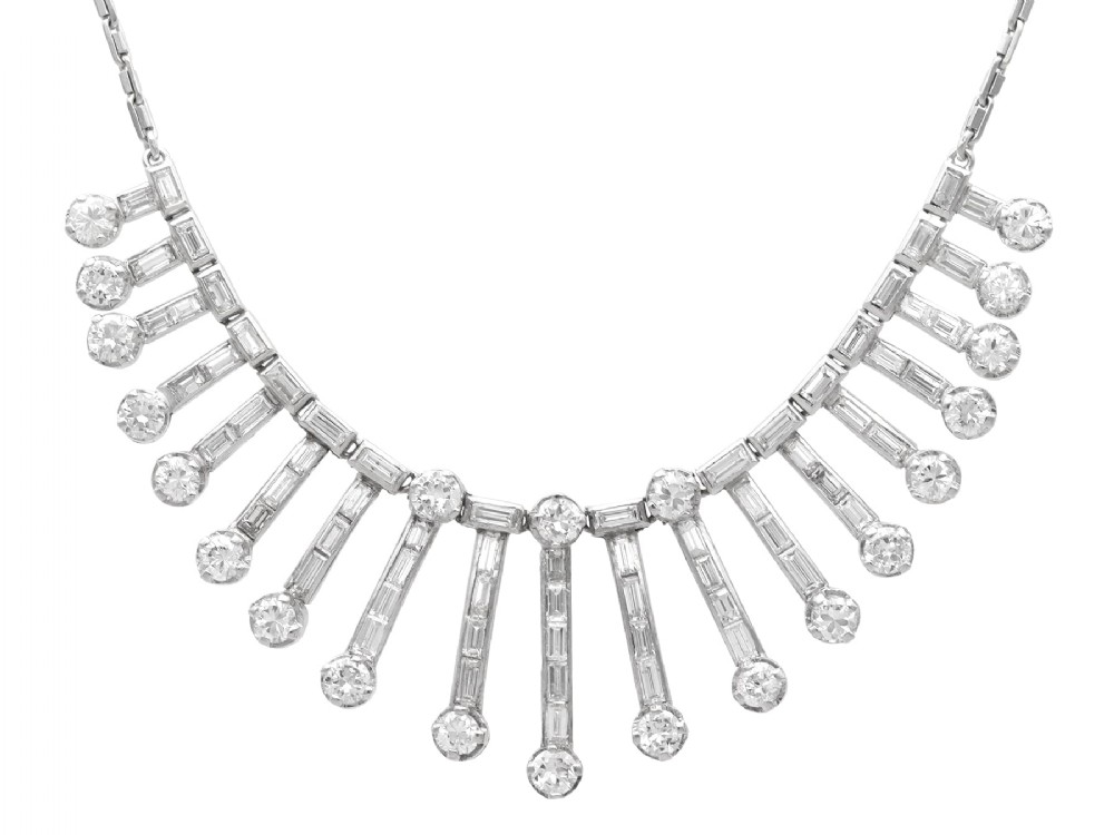 An Art Deco platinum fringe necklace set with baguette and round cut diamonds arranged in a geometric drop pattern.