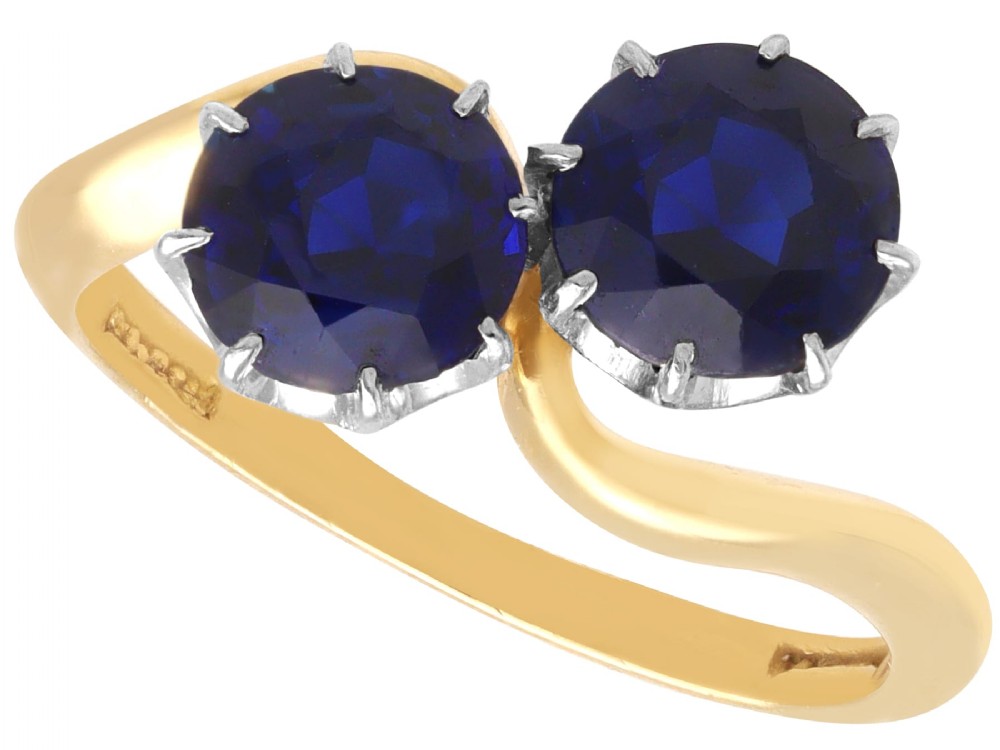 An 18ct yellow gold crossover twist ring featuring two round deep blue sapphires set in multi-claw settings.