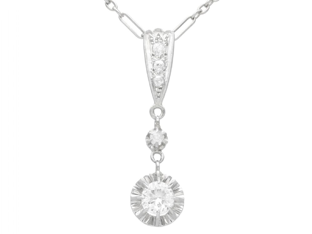 An Art Deco platinum drop pendant set with diamonds, featuring a decorative tapered top bail and suspended circular diamond setting on a fine link chain.
