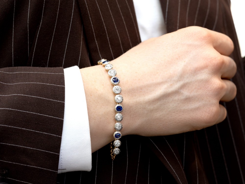 An Art Deco 18ct yellow gold line bracelet set with alternating oval blue sapphires and round diamonds featuring engraved bezel borders. View VI