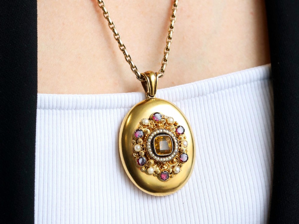 An oval 18ct yellow gold Victorian locket featuring a central yellow citrine surrounded by seed pearls, garnets, and detailed gold wirework. View IV
