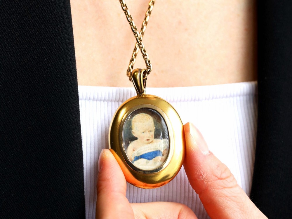 An oval 18ct yellow gold Victorian locket featuring a central yellow citrine surrounded by seed pearls, garnets, and detailed gold wirework. View VI