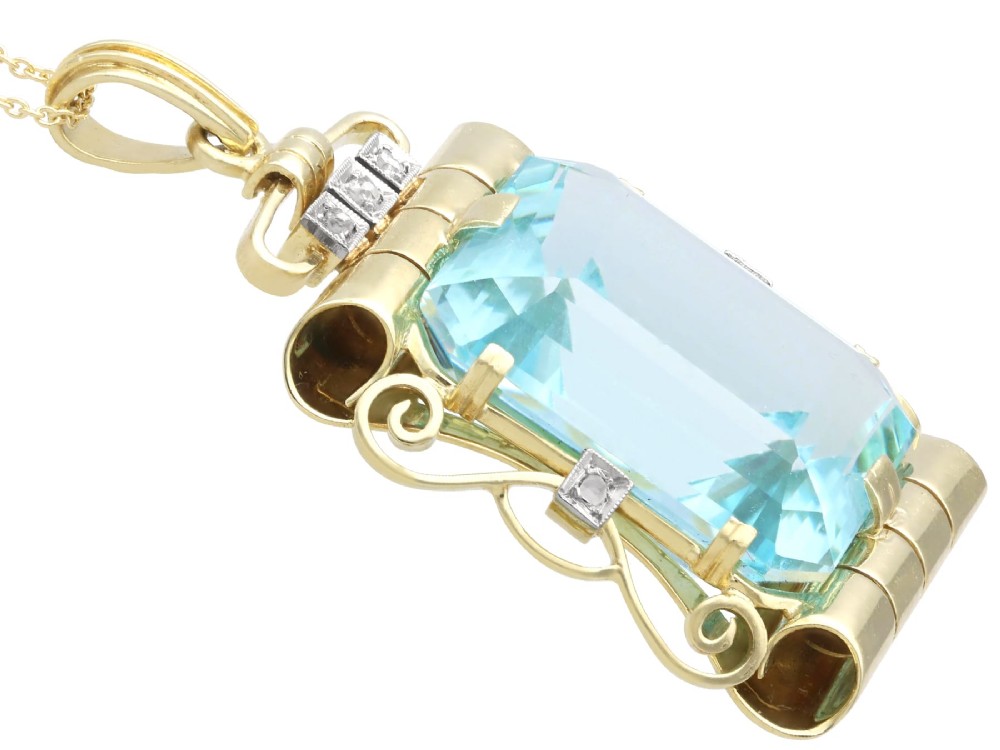 A large emerald-cut aquamarine gemstone mounted in a yellow gold scrollwork frame accented with small diamonds and suspended from a chain. View VIII