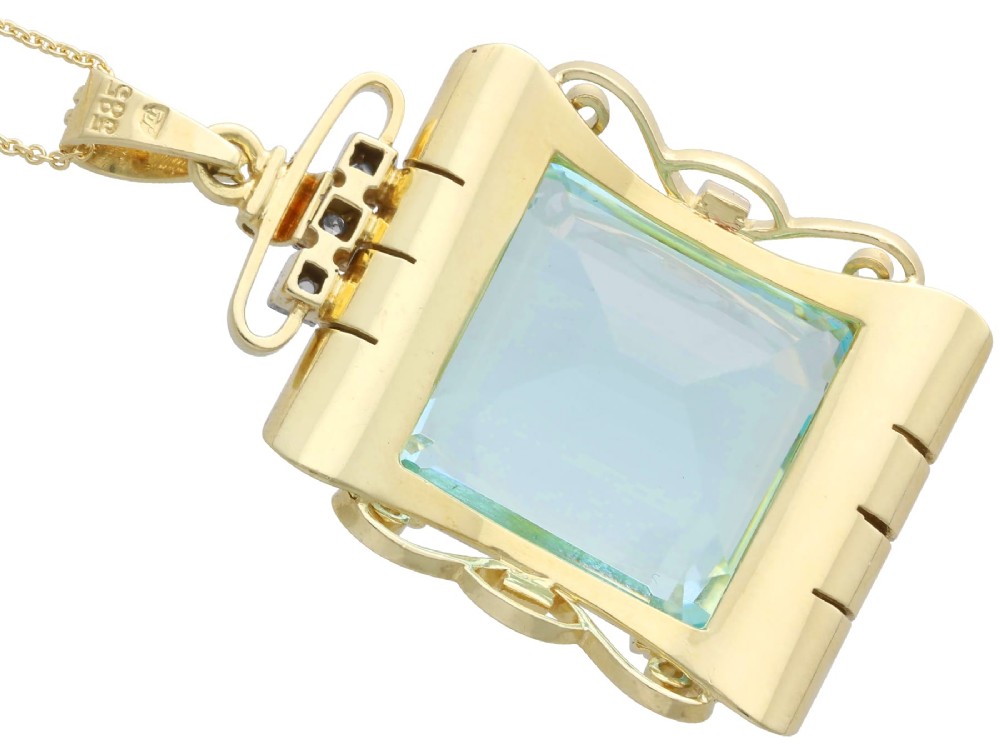 A large emerald-cut aquamarine gemstone mounted in a yellow gold scrollwork frame accented with small diamonds and suspended from a chain. View IX
