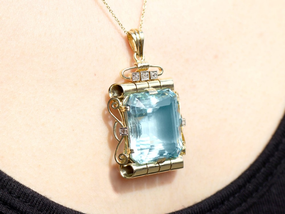 A large emerald-cut aquamarine gemstone mounted in a yellow gold scrollwork frame accented with small diamonds and suspended from a chain. View XIII