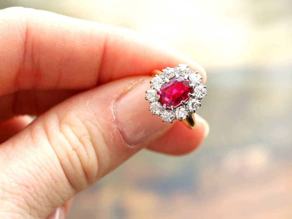 An antique 18ct yellow gold ring featuring a central oval red ruby set within a cluster halo of round white diamonds. View IV