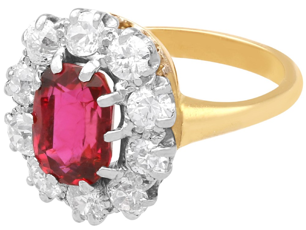 An antique 18ct yellow gold ring featuring a central oval red ruby set within a cluster halo of round white diamonds. View VI