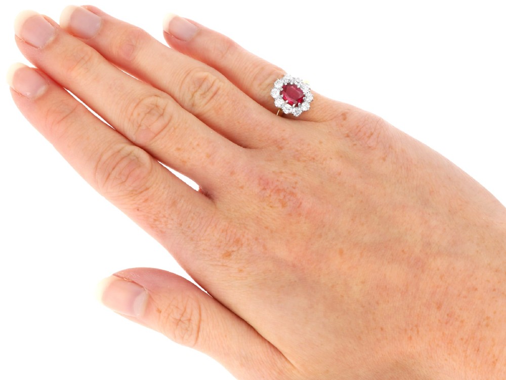An antique 18ct yellow gold ring featuring a central oval red ruby set within a cluster halo of round white diamonds. View X