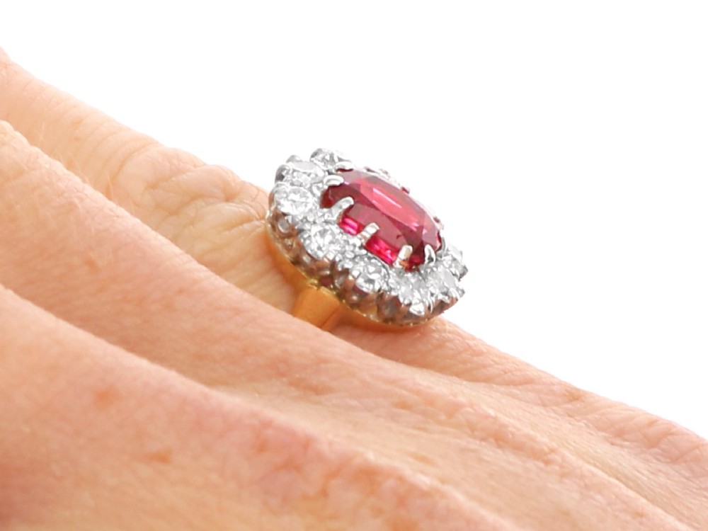 An antique 18ct yellow gold ring featuring a central oval red ruby set within a cluster halo of round white diamonds. View XI