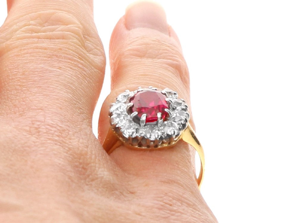 An antique 18ct yellow gold ring featuring a central oval red ruby set within a cluster halo of round white diamonds. View XII