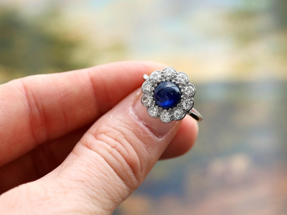 A platinum ring set with a central round cabochon blue sapphire surrounded by a halo of ten round diamonds. View V