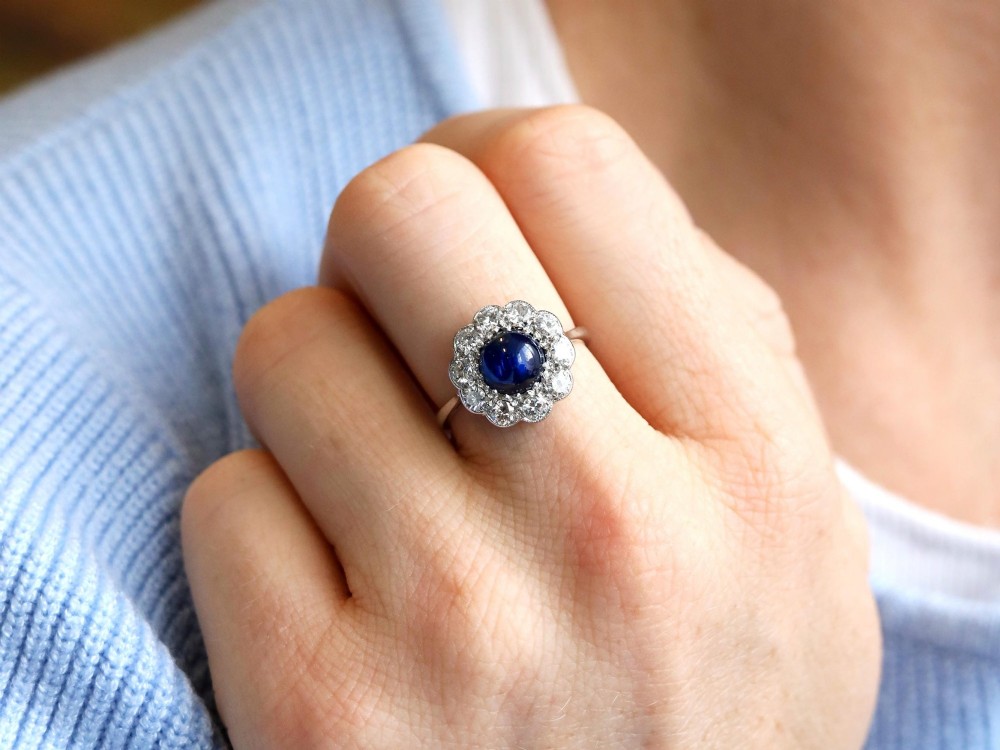 A platinum ring set with a central round cabochon blue sapphire surrounded by a halo of ten round diamonds. View VI