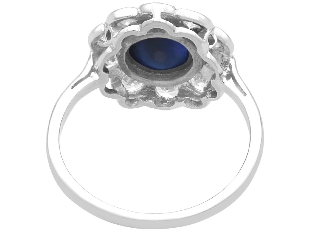 A platinum ring set with a central round cabochon blue sapphire surrounded by a halo of ten round diamonds. View VIII