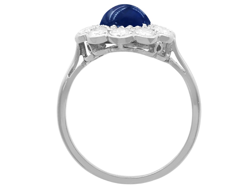 A platinum ring set with a central round cabochon blue sapphire surrounded by a halo of ten round diamonds. View IX