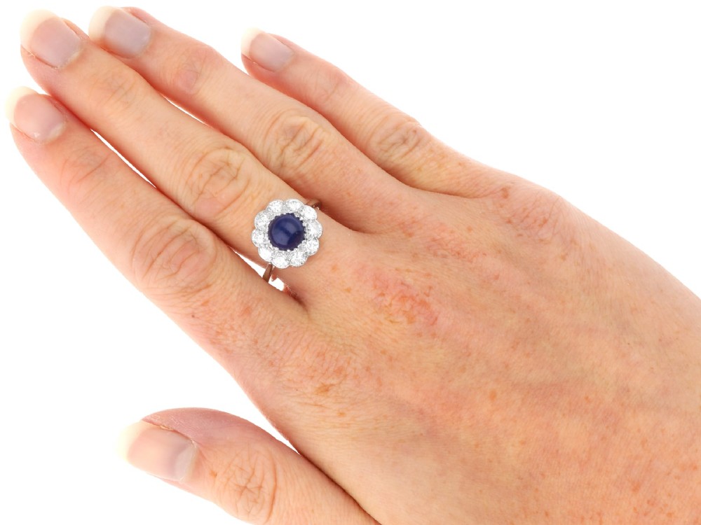 A platinum ring set with a central round cabochon blue sapphire surrounded by a halo of ten round diamonds. View X