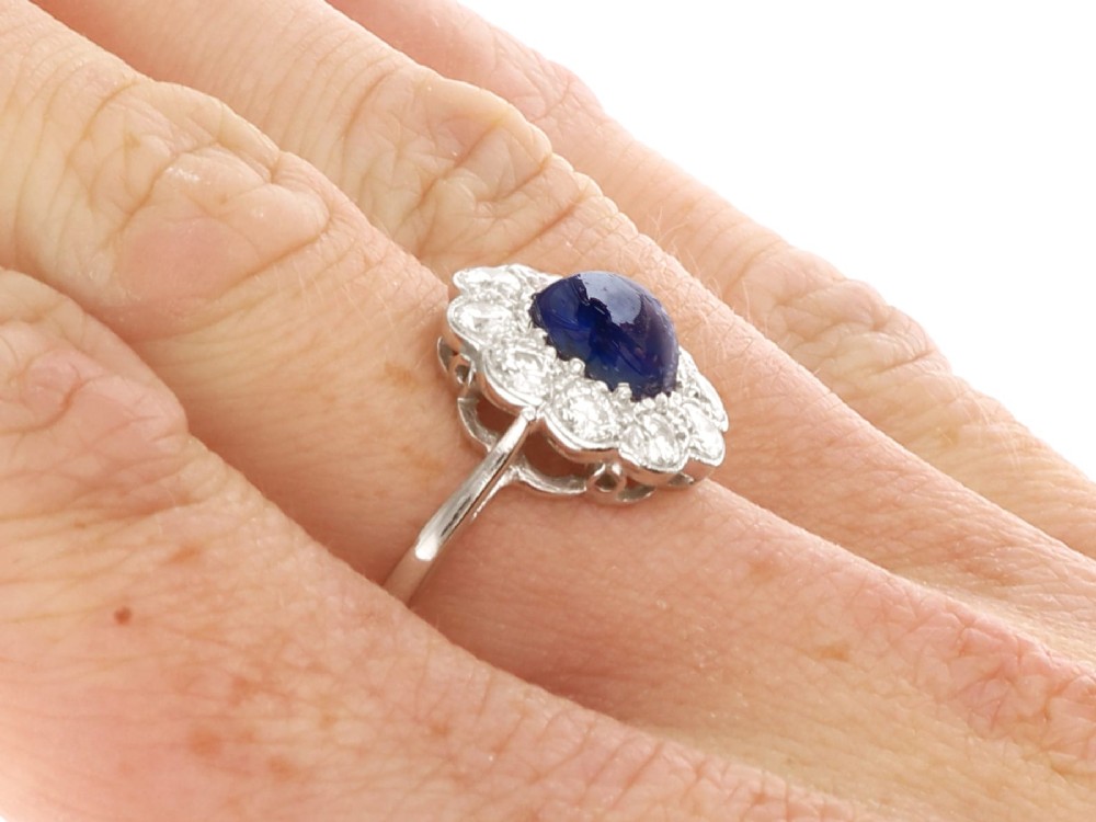 A platinum ring set with a central round cabochon blue sapphire surrounded by a halo of ten round diamonds. View XI