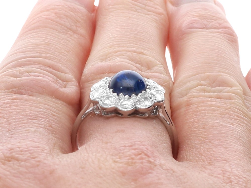 A platinum ring set with a central round cabochon blue sapphire surrounded by a halo of ten round diamonds. View XII