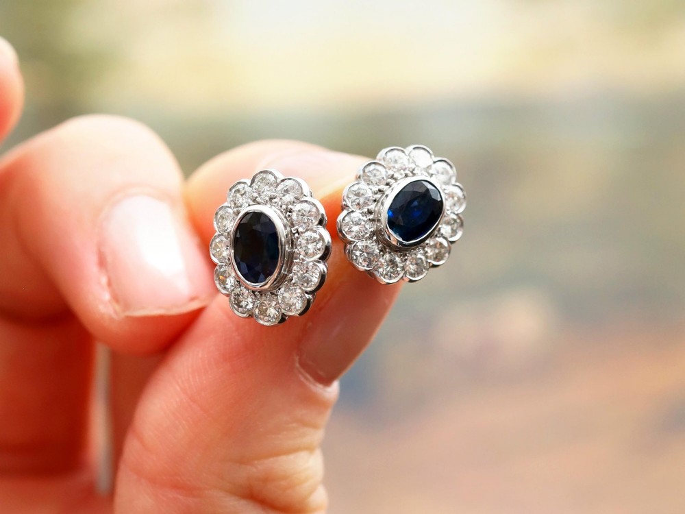Pair of 1930s 18ct white gold cluster earrings featuring oval blue sapphire centerpieces framed by halos of round diamonds. View V