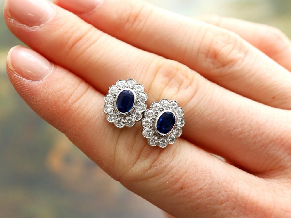 Pair of 1930s 18ct white gold cluster earrings featuring oval blue sapphire centerpieces framed by halos of round diamonds. View VI