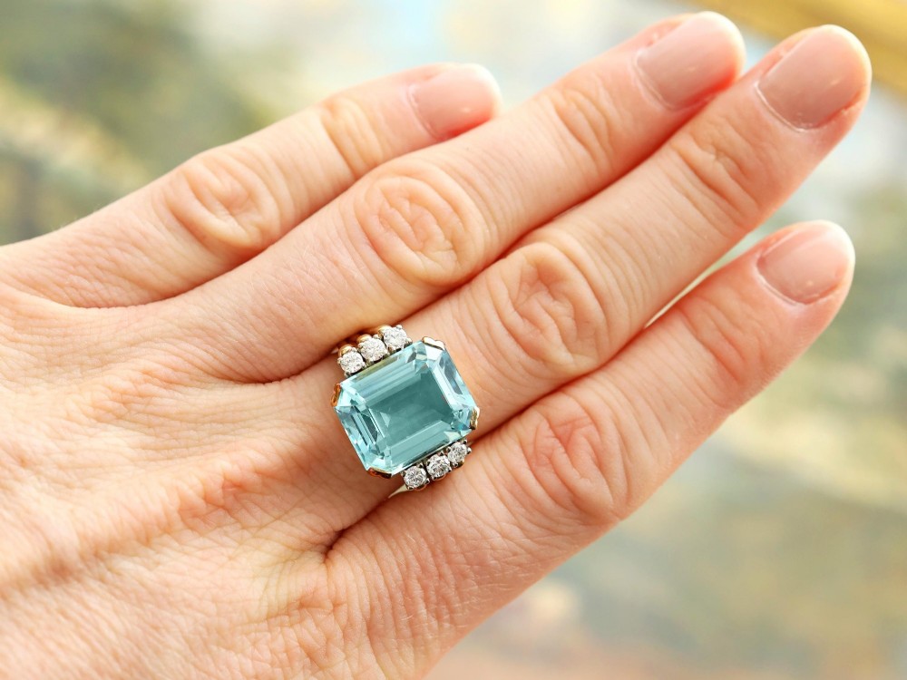 A 14ct yellow gold dress ring featuring a large emerald-cut light blue aquamarine central gemstone flanked by six round diamonds. View VI