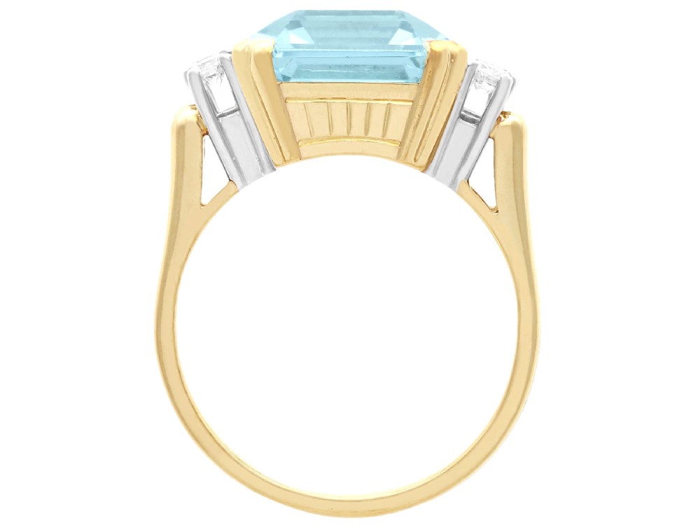 A 14ct yellow gold dress ring featuring a large emerald-cut light blue aquamarine central gemstone flanked by six round diamonds. View X