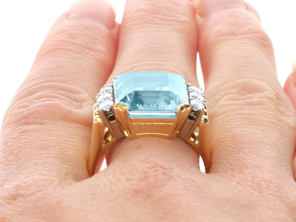 A 14ct yellow gold dress ring featuring a large emerald-cut light blue aquamarine central gemstone flanked by six round diamonds. View XV