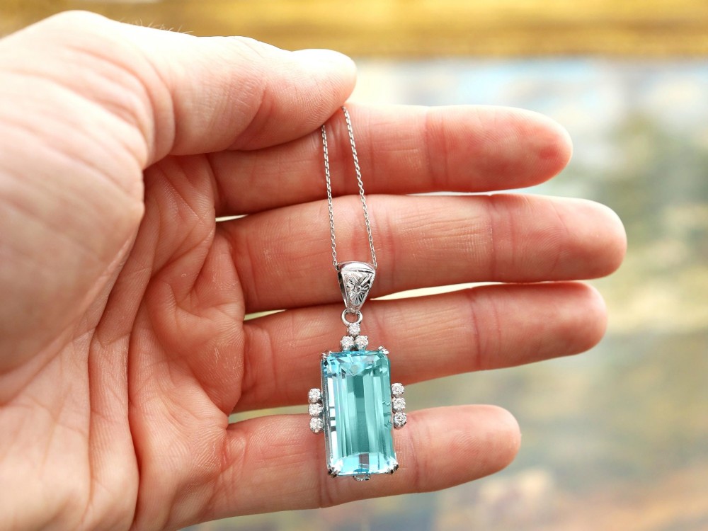 A vintage 18ct white gold pendant featuring a large emerald-cut light blue aquamarine framed by accent diamonds, suspended from an engraved bail. View V