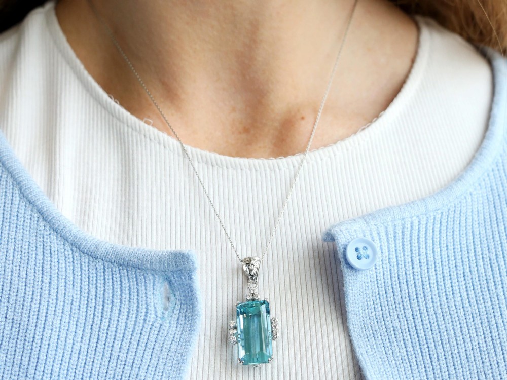 A vintage 18ct white gold pendant featuring a large emerald-cut light blue aquamarine framed by accent diamonds, suspended from an engraved bail. View VI