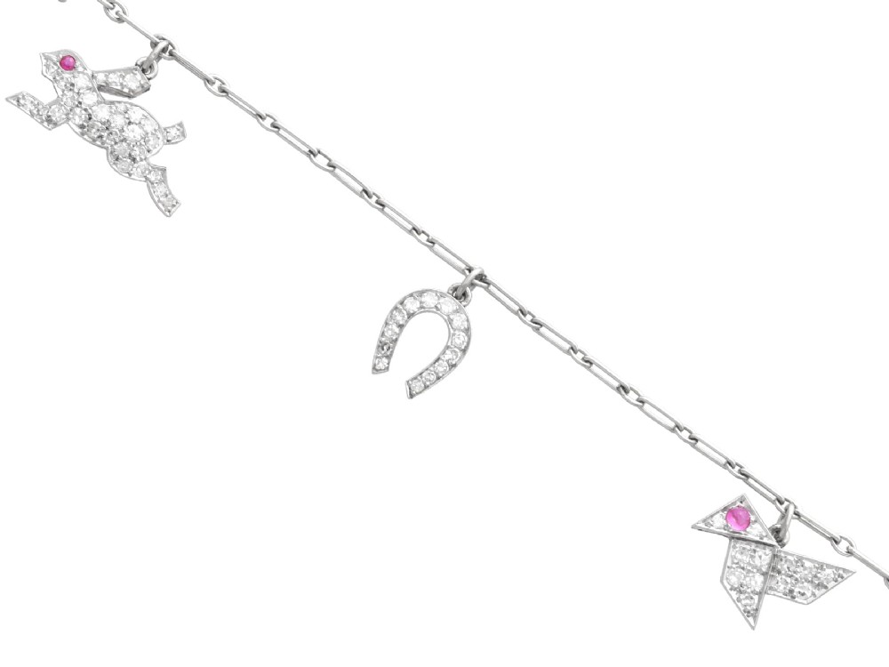 An antique platinum link chain charm bracelet featuring diamond-set charms including a running hare, a horseshoe, and a bird with ruby accents.
