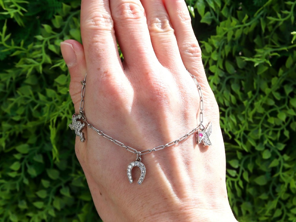An antique platinum link chain charm bracelet featuring diamond-set charms including a running hare, a horseshoe, and a bird with ruby accents. View II