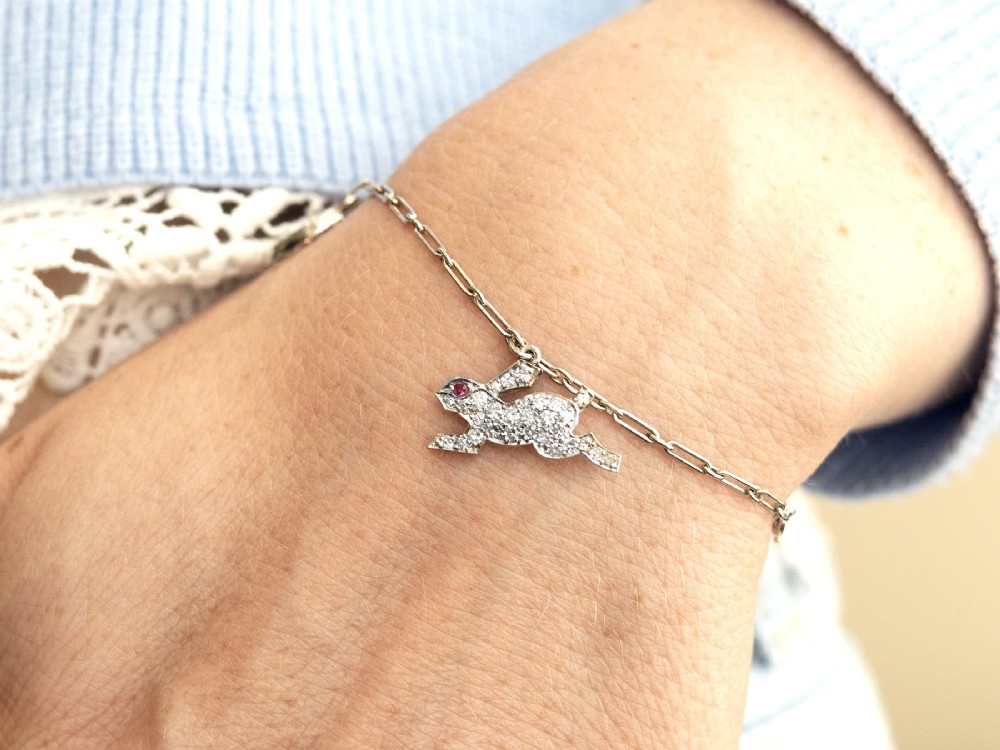 An antique platinum link chain charm bracelet featuring diamond-set charms including a running hare, a horseshoe, and a bird with ruby accents. View III