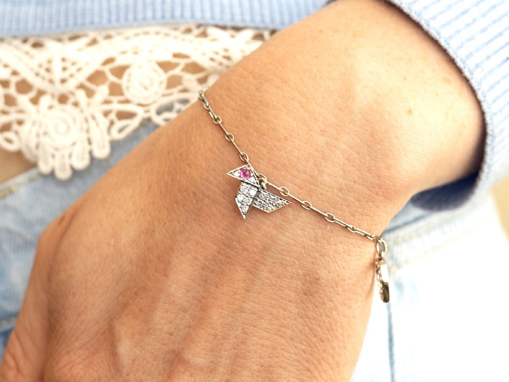 An antique platinum link chain charm bracelet featuring diamond-set charms including a running hare, a horseshoe, and a bird with ruby accents. View IV