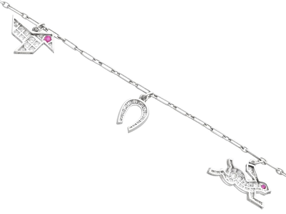 An antique platinum link chain charm bracelet featuring diamond-set charms including a running hare, a horseshoe, and a bird with ruby accents. View VIII