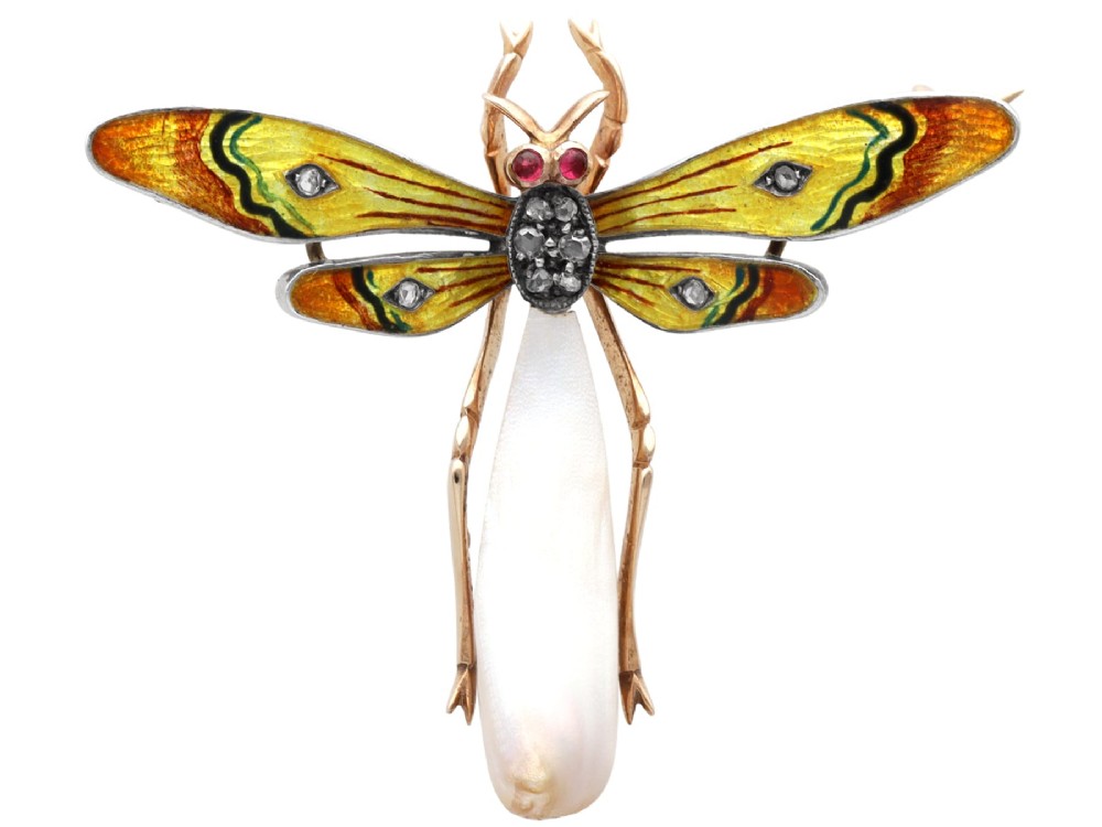 An antique late Victorian dragonfly brooch crafted in yellow gold with yellow enamel wings, garnet eyes, rose-cut diamond accents, and a elongated natural pearl abdomen.