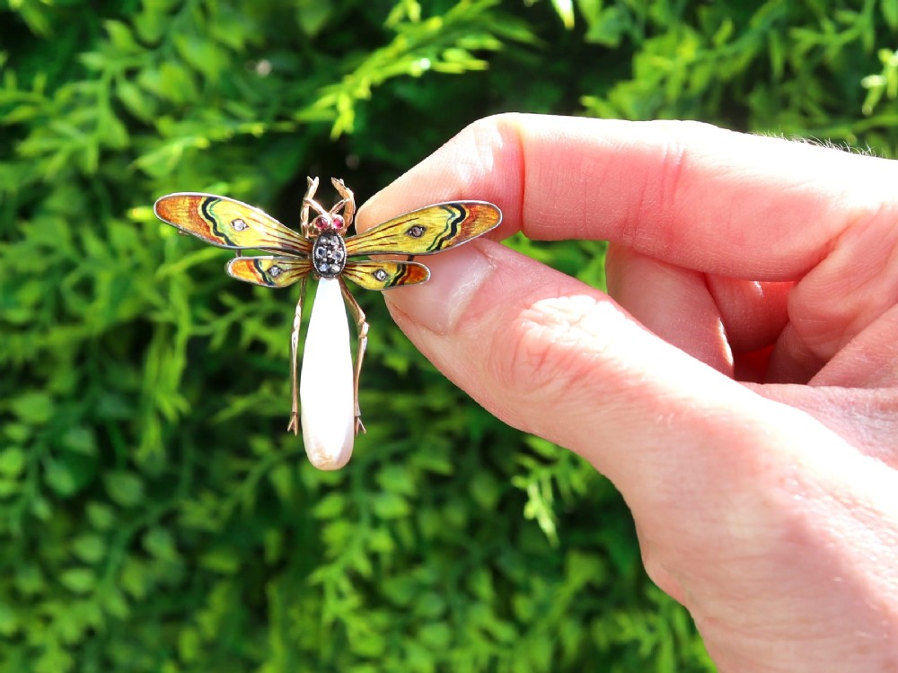 An antique late Victorian dragonfly brooch crafted in yellow gold with yellow enamel wings, garnet eyes, rose-cut diamond accents, and a elongated natural pearl abdomen. View II